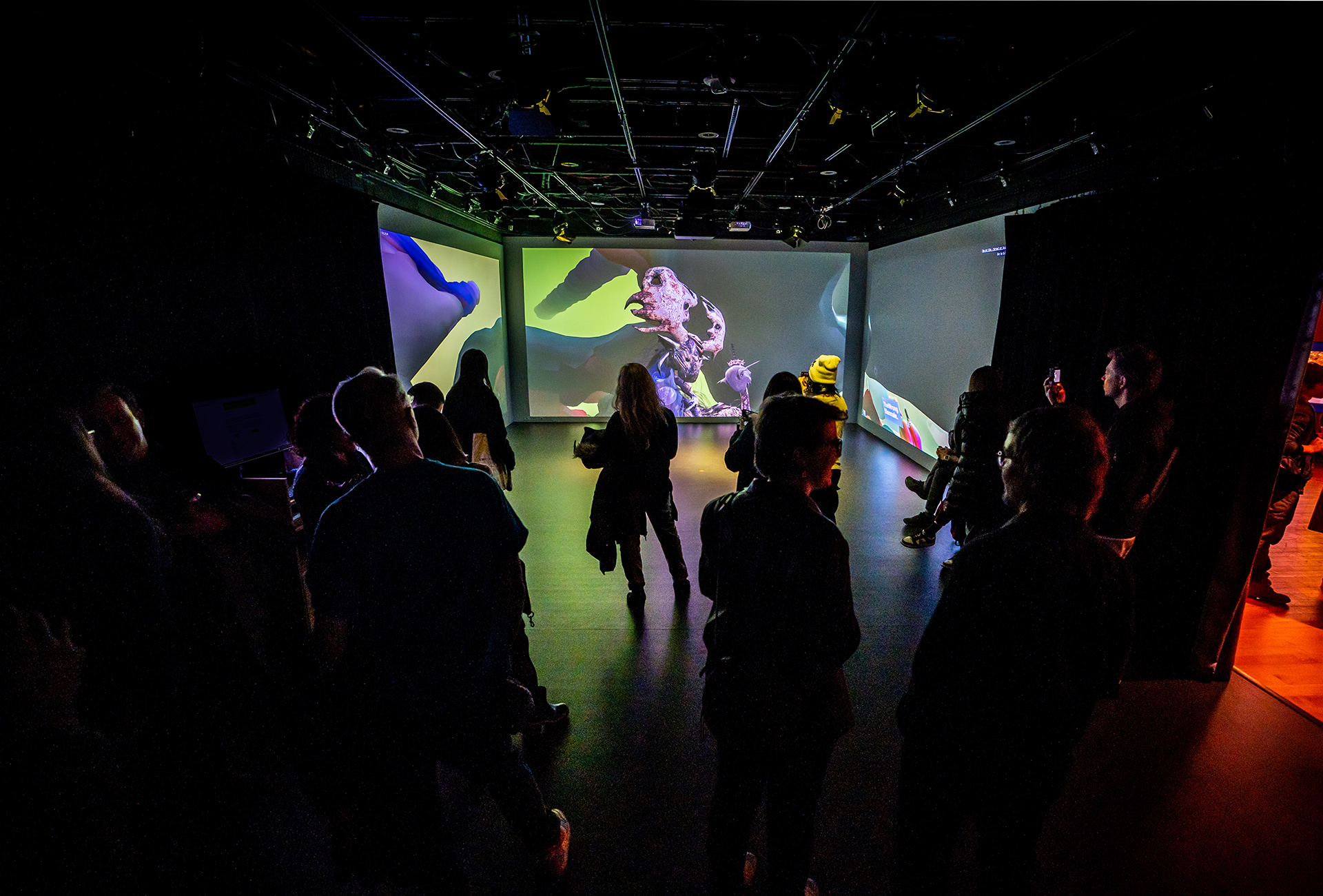 Several visitors to the exhibition viewing a large three channel 3d installation'